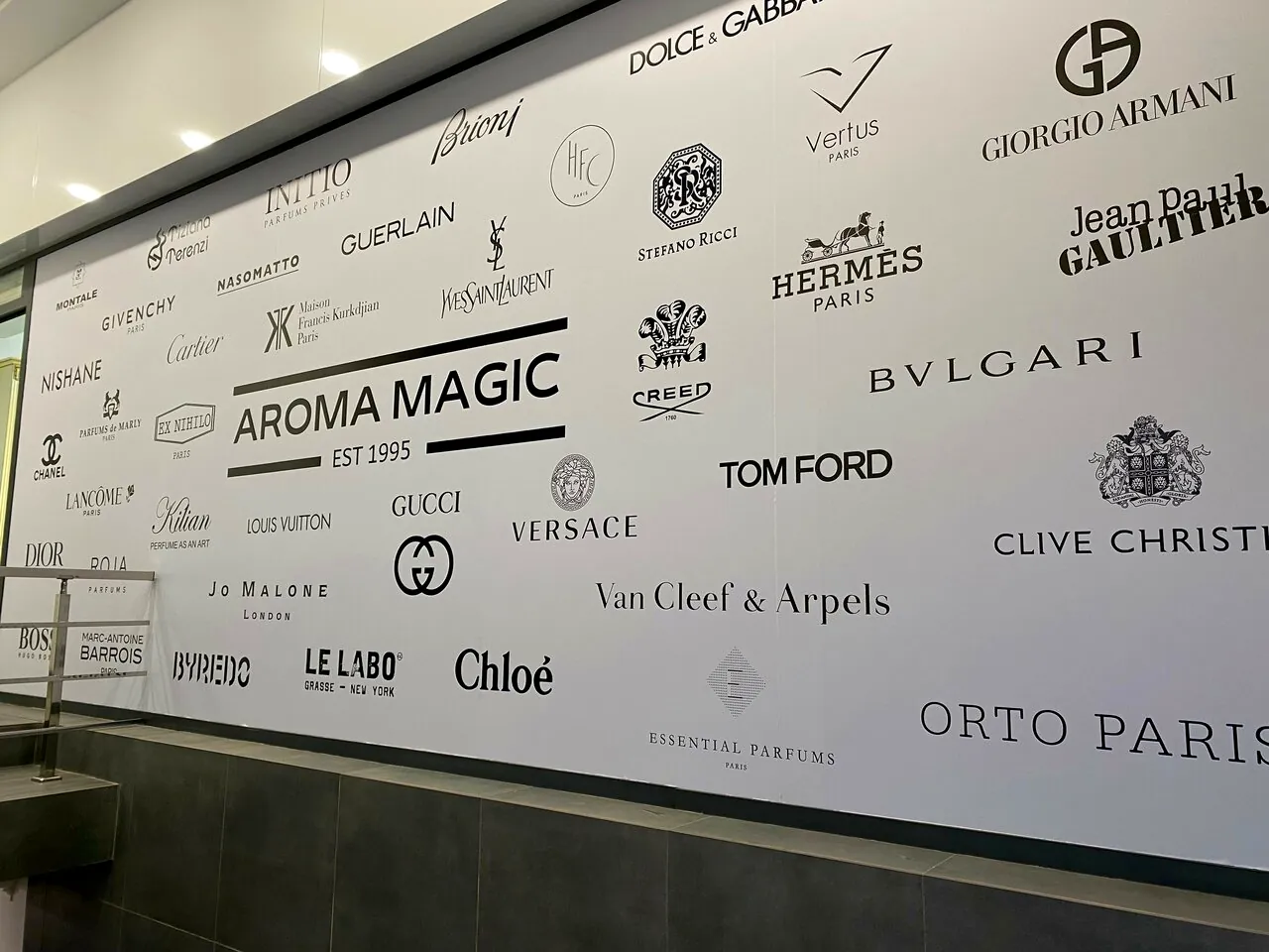 Стена домов в магазине: AROMA MAGIC EST 1995 среди логотипов Chanel, Hermès, Bvlgari, Tom Ford