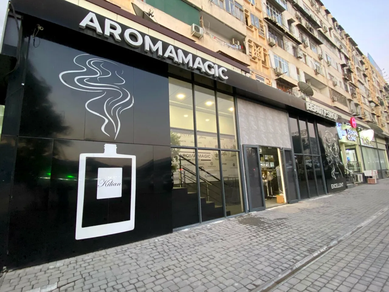 Вход в магазин Aroma Magic: чёрный фасад с вывеской AROMAMAGIC и световым флаконом Kilian
